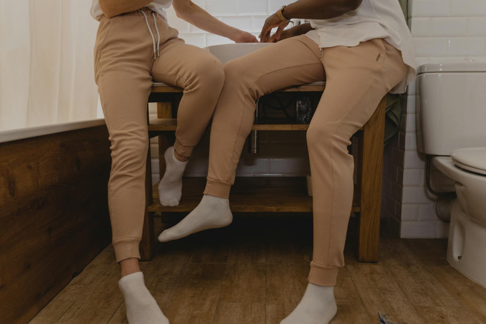 Two people in matching joggers and socks sit comfortably indoors, showcasing casual fashion.