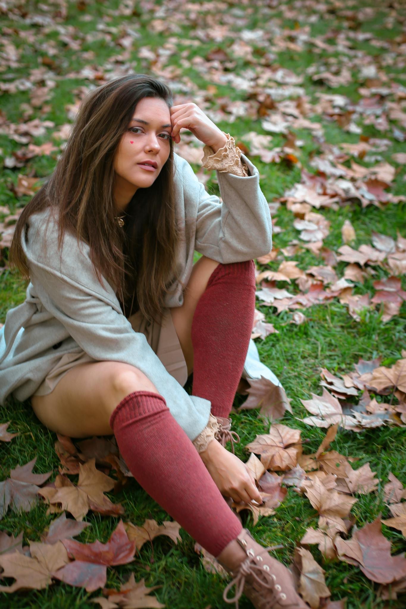 Woman in cozy fall attire poses among fallen leaves, showcasing autumn fashion.